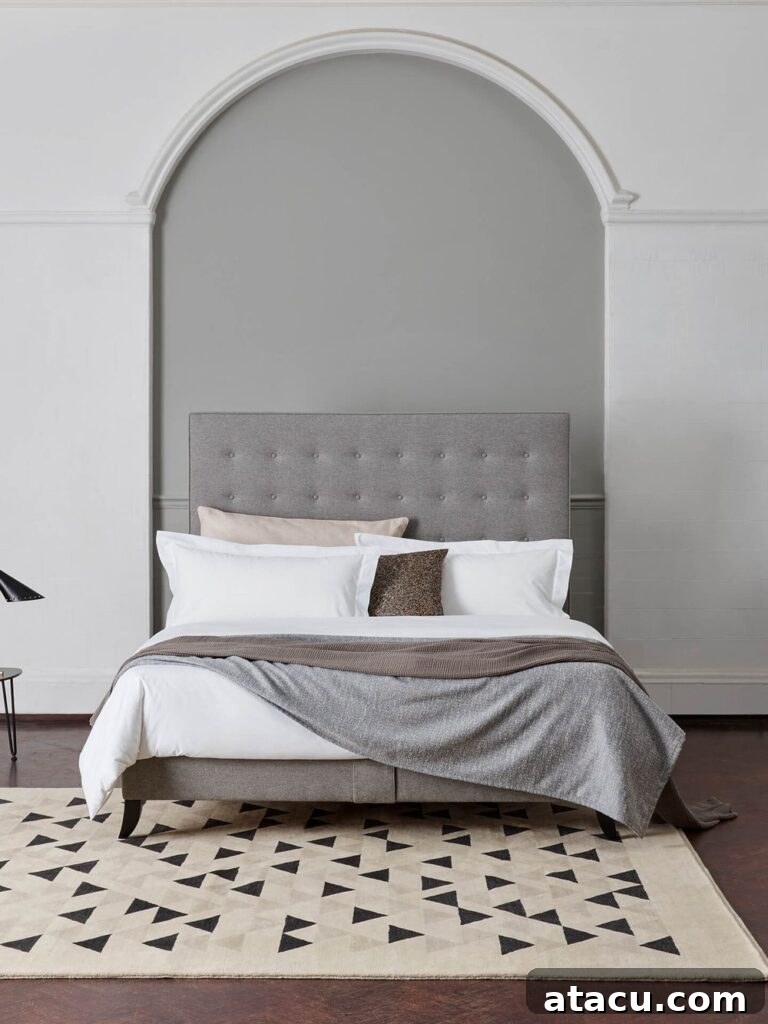 Luxurious white bed sheets on a large bed with a sophisticated grey padded headboard, suggesting comfort and elegance.