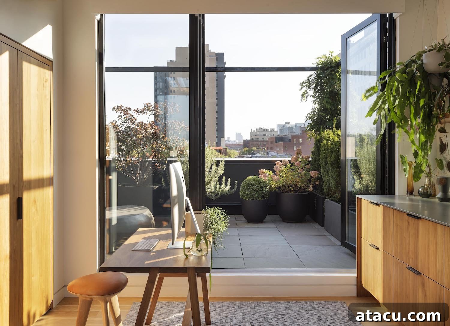 Minimalist home office with natural wood desk, comfortable chair, and a large window overlooking greenery.