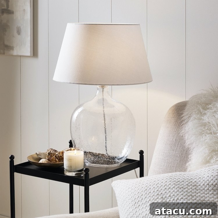 A glass table lamp in a neutral coloured living room. The lamp features an organic bubble-textured base and a simple white linen shade.