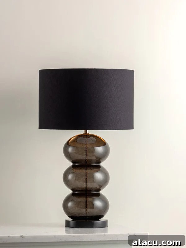 Seki smoked glass table lamp with a matt black metal base and a black drum shade with a brass lining.