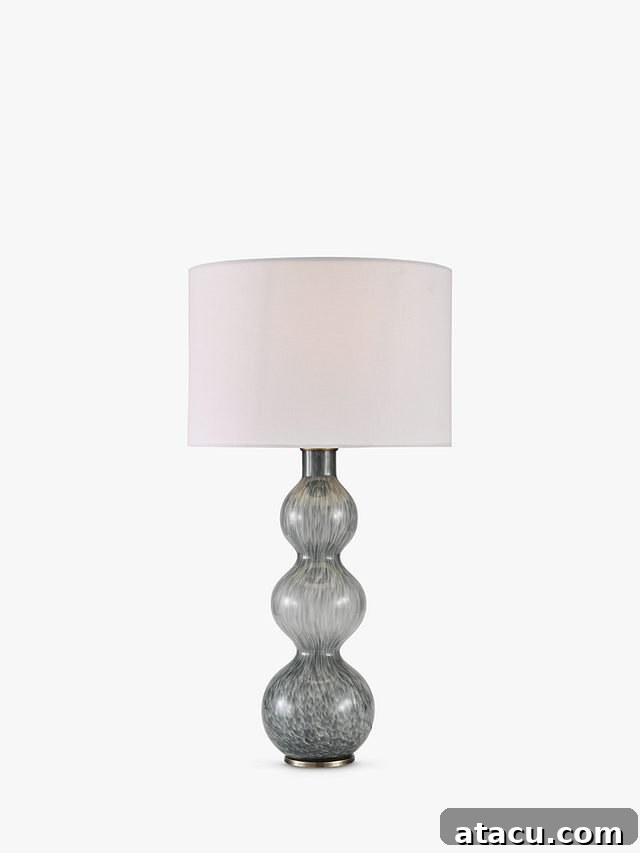 A mottled grey glass table lamp with a tall sculptural form and a simple white shade.