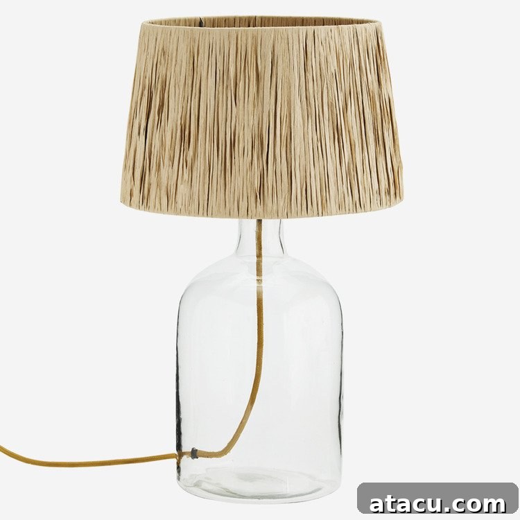 Large glass table lamp with a bottle shaped base and a natural raffia shade for a modern rustic look.