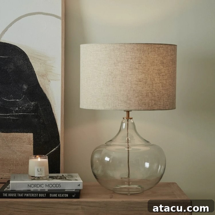 A glass table lamp with a bulbous form, brass-coloured fittings, and a natural cotton shade.