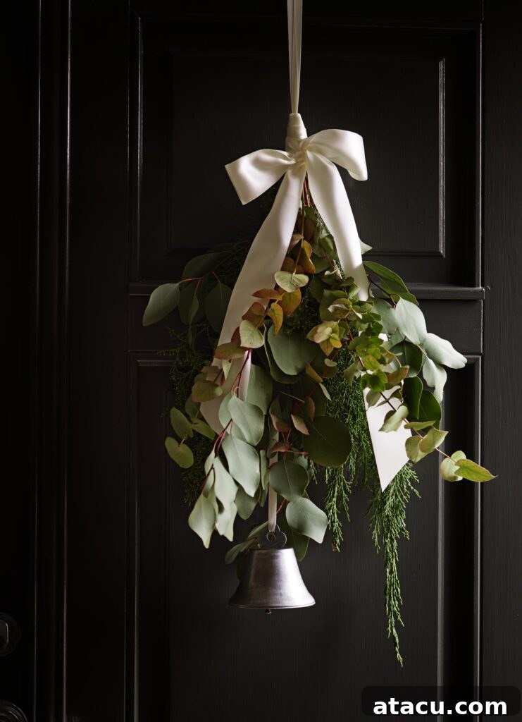 A simple eucalyptus garland gracefully hanging on a black door, accented with a white bow and a small bell for natural Christmas elegance.