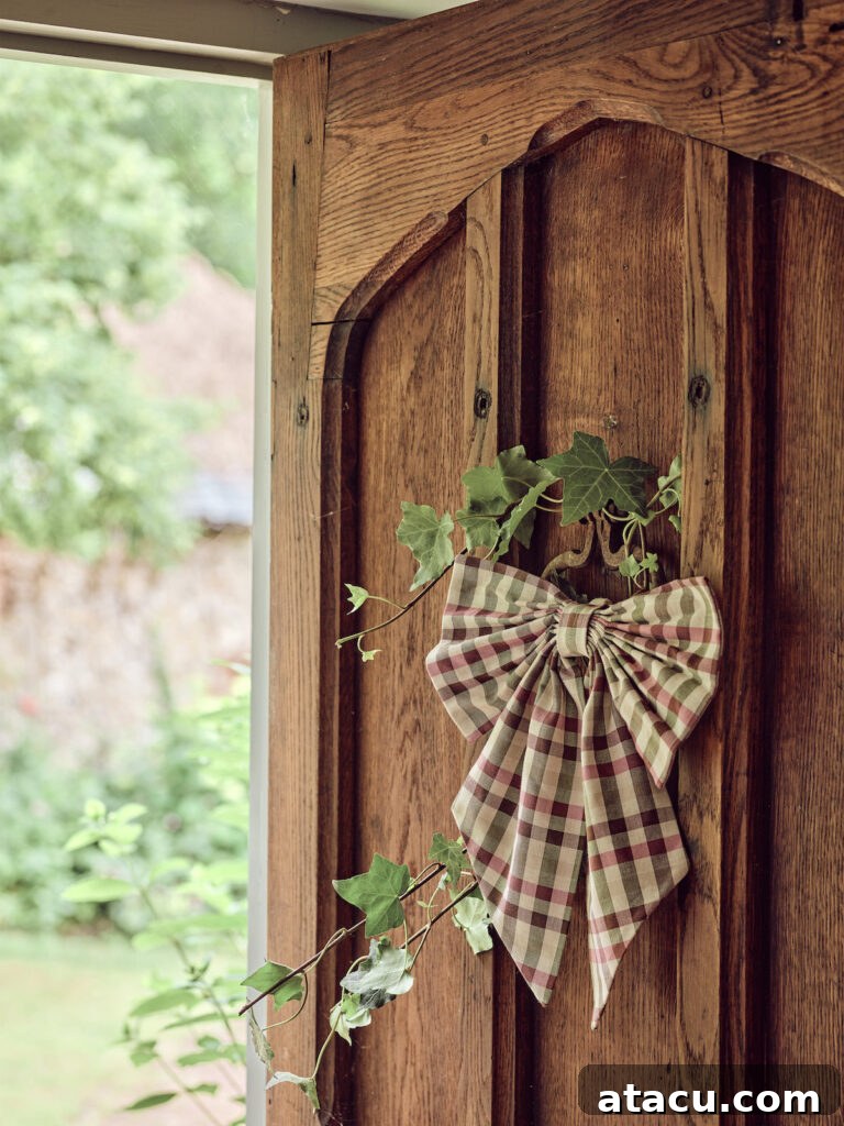 A charming checked Christmas door bow and an ivy garland adorning a rustic wooden cottage-style front door, celebrating natural festive decor.