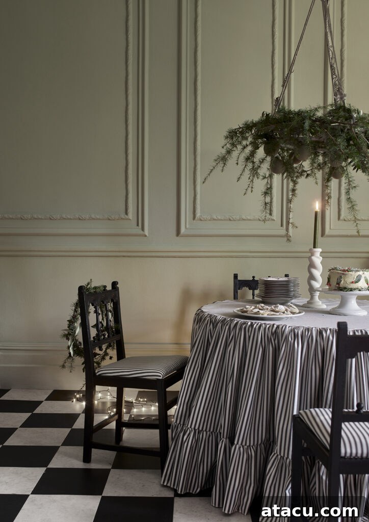 A beautifully decorated Christmas table with a striped tablecloth, a lush greenery wreath as a centerpiece, and a long hanging garland above, all illuminated by candle light.
