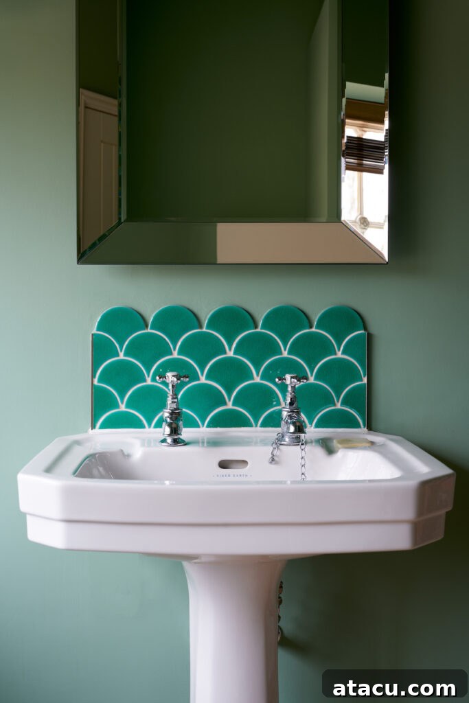 Vibrant emerald green fish scale tiles forming a stunning backsplash above a pedestal sink in a stylish green bathroom.