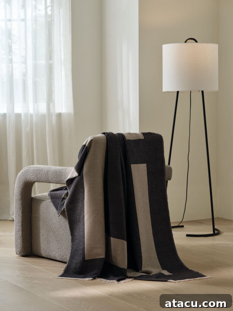 A luxurious cream boucle armchair draped with a soft, textured throw next to a sleek, modern floor lamp, set in a tranquil neutral-toned room. This inviting scene highlights comfort and refined minimalist design.