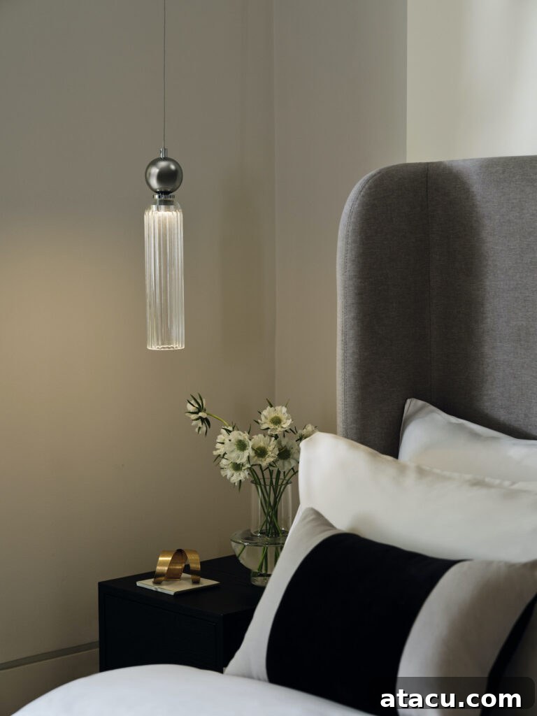 A sophisticated bedroom featuring a sleek glass pendant light suspended above a minimalist bedside table. The room boasts a calming neutral colour palette, enhancing the modern luxury aesthetic.