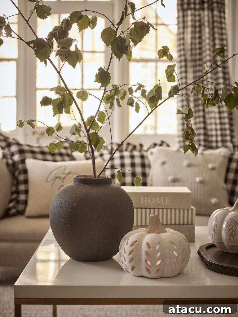 A white ceramic pumpkin tealight holder for Halloween and a grey vase on a coffee table in an elegant modern country style living room with gingham cushions and curtains.
