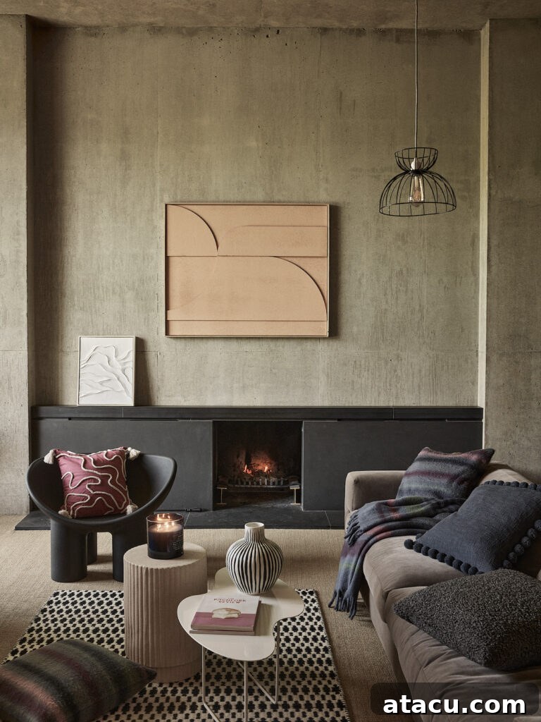Modern cosy living room with a minimalist concrete wall, a fireplace, and abstract wall art. A black accent chair with a patterned pillow sits beside a beige sofa with a dark throw blanket, creating a cosy atmosphere.