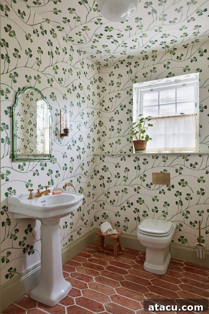 Charming cloakroom with whimsical green botanical wallpaper covering walls and ceiling, paired with rustic terracotta floor tiles. Features a vintage pedestal sink with brass taps, a decorative mirror, and a small plant on a windowsill.