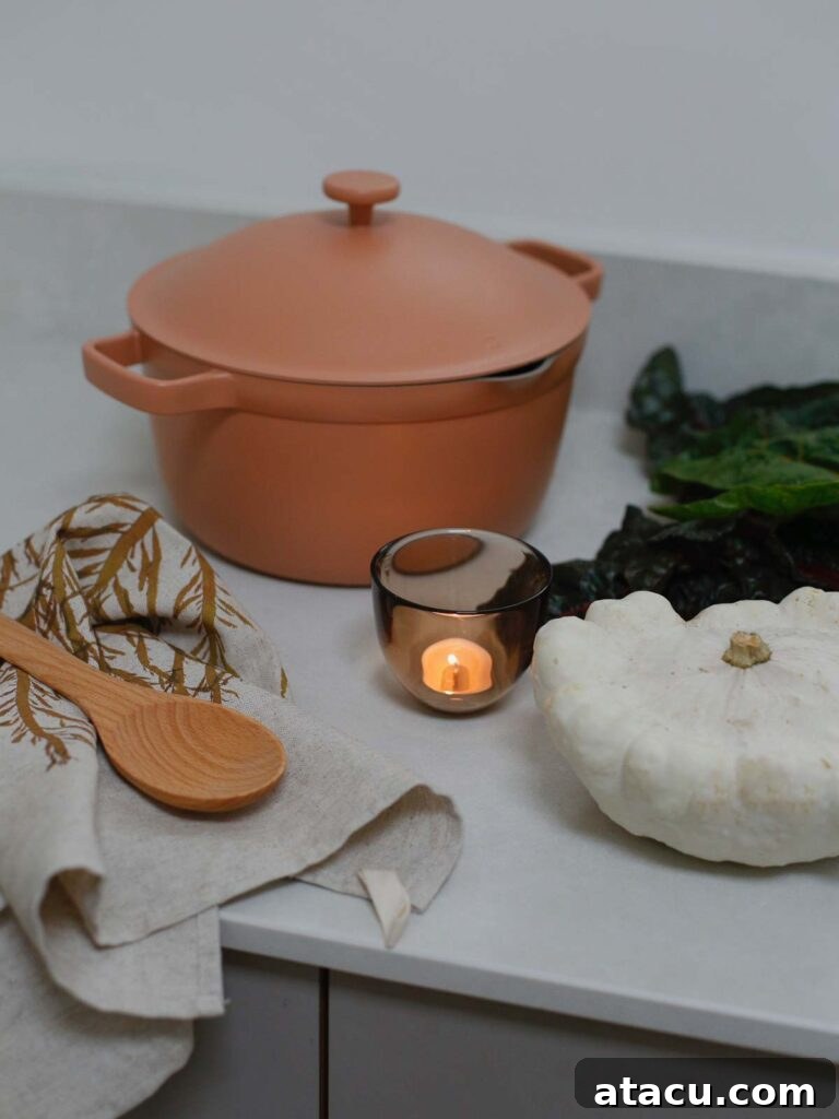 "Earthy kitchen decor with a pink Our Place Perfect Pot, candlelight, white pumpkin, and fall vegetables on the countertop.