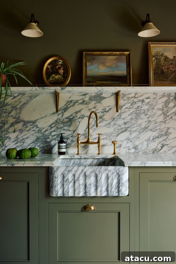 A sophisticated kitchen with sage green cabinetry, a fluted marble farmhouse sink, brass fixtures, and a marble backsplash, styled with vintage artwork and warm lighting.