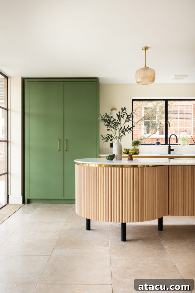 
A stylish kitchen featuring sage green cabinets, a fluted wood island with gold accents, and natural light streaming through black-framed windows.