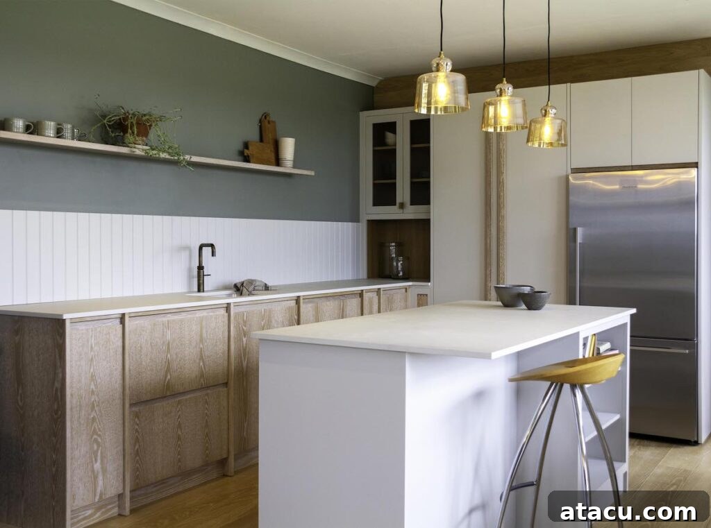 A contemporary kitchen with brushed lime grain oak cabinetry, a sleek white island, and a sage green wall. The space features open shelving, brass pendant lights, and a stainless steel refrigerator for a modern yet natural look.
