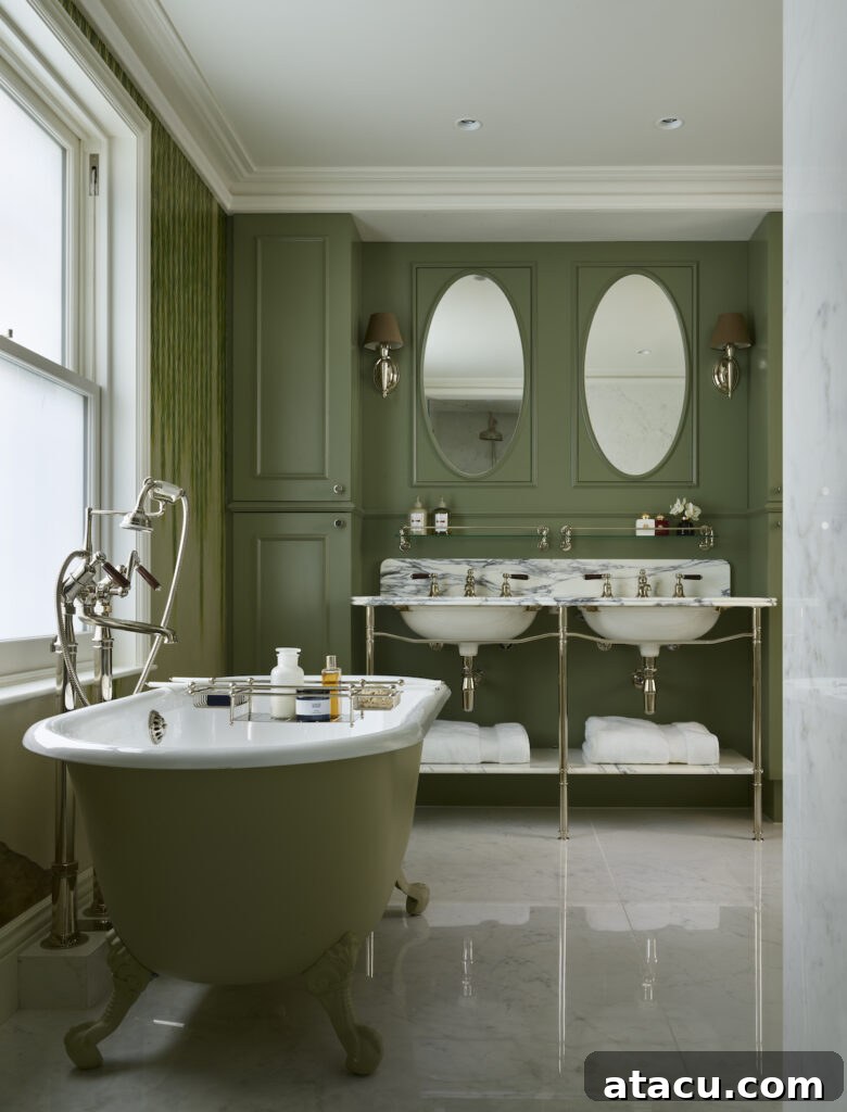 An opulent Victorian style bathroom featuring a sage green cast-iron tub, polished nickel fixtures, a marble double vanity, and intricate de Gournay wallpaper.