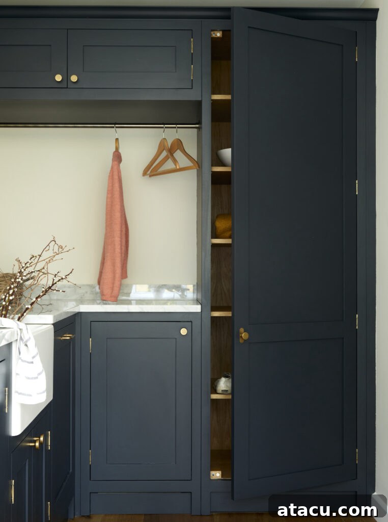 Laundry room upstairs featuring navy cabinetry with brass accents, open shelving for storage, a hanging rail for clothes, and a marble countertop for folding and organisation.