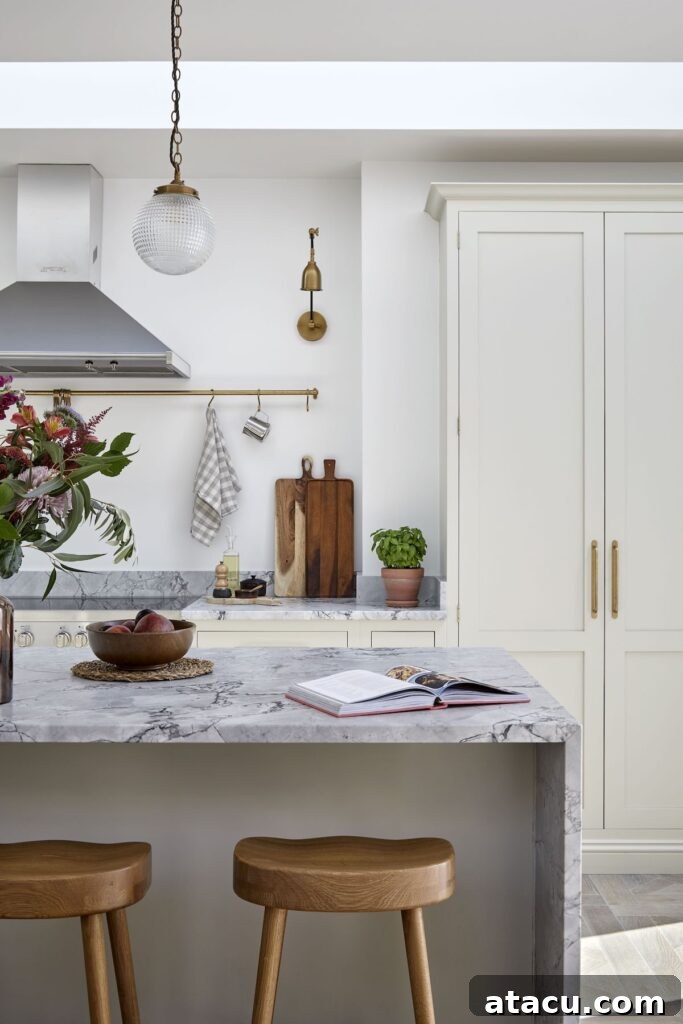 Cream shaker kitchen with two stools arranged under a marble waterfall island.