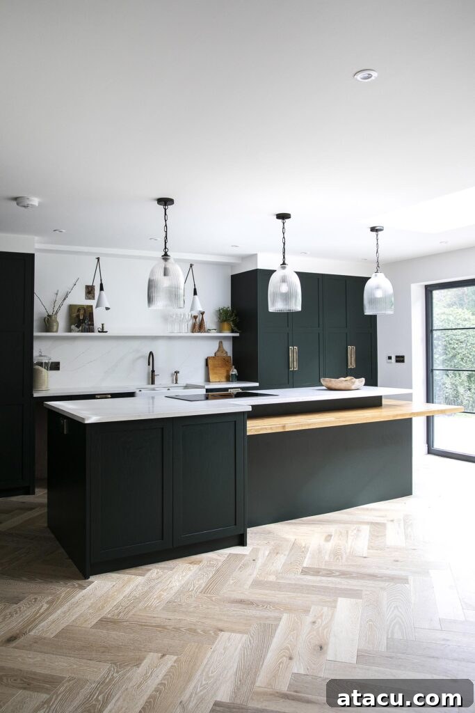 A stylish kitchen featuring a modern multi-level kitchen island with a sleek white countertop and warm wood extension, surrounded by dark cabinetry and illuminated by elegant pendant lighting.