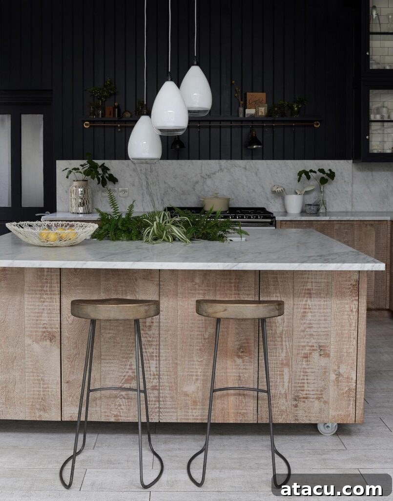 A light wood kitchen island on wheels with glass pendant lighting hanging above in a black painted kitchen.
