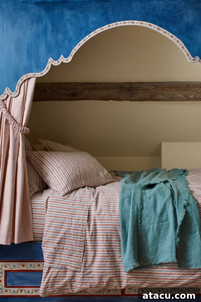 Cozy arched bed nook with a painted blue arch, striped bedding, and a soft teal throw for a layered look. An exposed wooden beam adds rustic character.