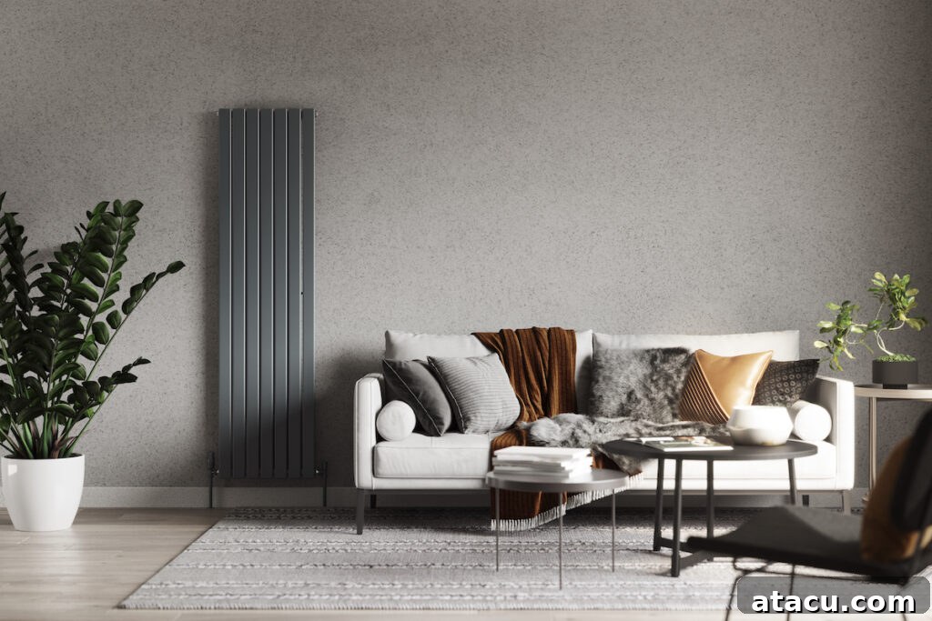 A modern living room featuring a sleek vertical radiator in a muted gray tone, blending seamlessly with the textured wall. The cozy white sofa is styled with layered cushions and a warm throw, creating a snug atmosphere. Accents of greenery and a soft area rug complete this stylish space, showcasing home heating hacks that maximize both comfort and design.