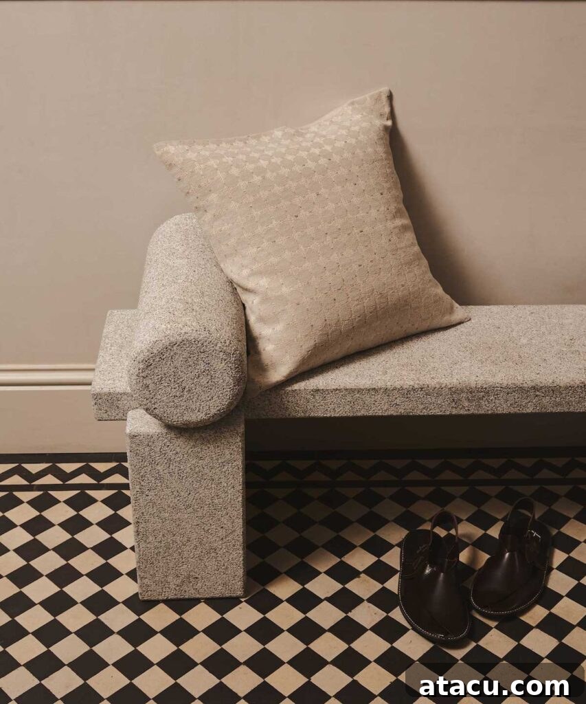 A geometric stone bench featuring a soft neutral cushion, styled with a patterned floor and simple black sandals for a modern neutral home decor aesthetic.