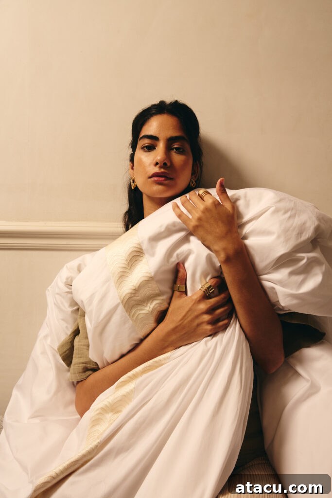 A woman embracing a luxurious white duvet with delicate gold embroidery, showcasing high quality bedding.