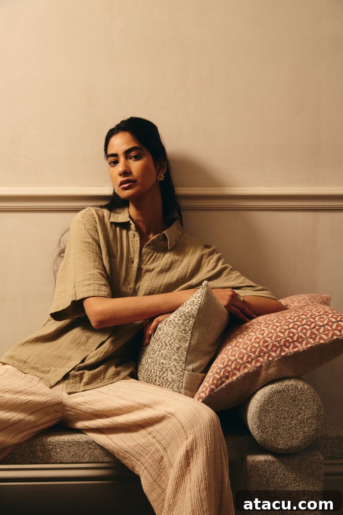 A woman sitting on a textured stone bench, surrounded by patterned throw pillows in warm tones, embodying cozy living room essentials.