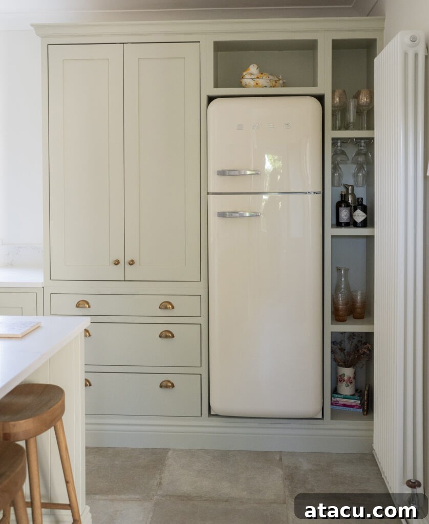 Small kitchen with built-in sage green cabinets, brass hardware, and a retro cream fridge, highlighting space-saving appliance integration.