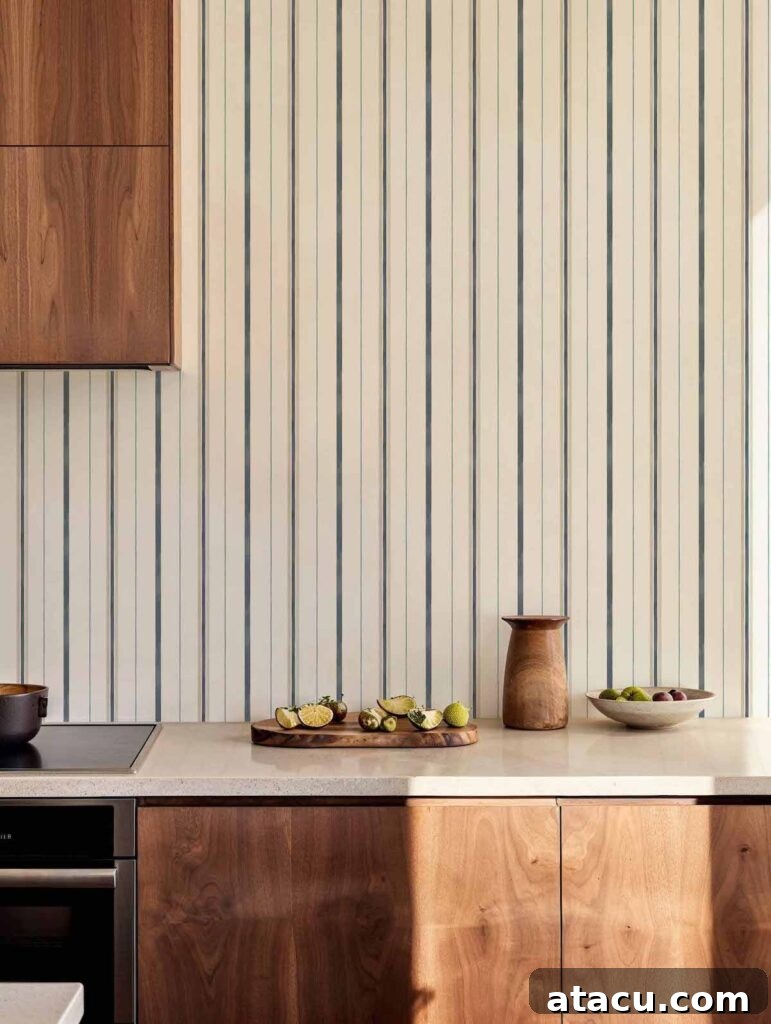 A kitchen with warm wood cabinetry, a neutral countertop, and striped wallpaper with fluid vertical lines.