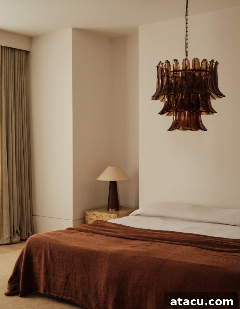 A cozy bedroom with a magnolia and rust color scheme, featuring a rust-colored linen bedspread, neutral-toned walls, and soft beige curtains. A vintage-inspired amber glass chandelier and a burl wood nightstand with a warm-toned lamp add texture and warmth to the space.