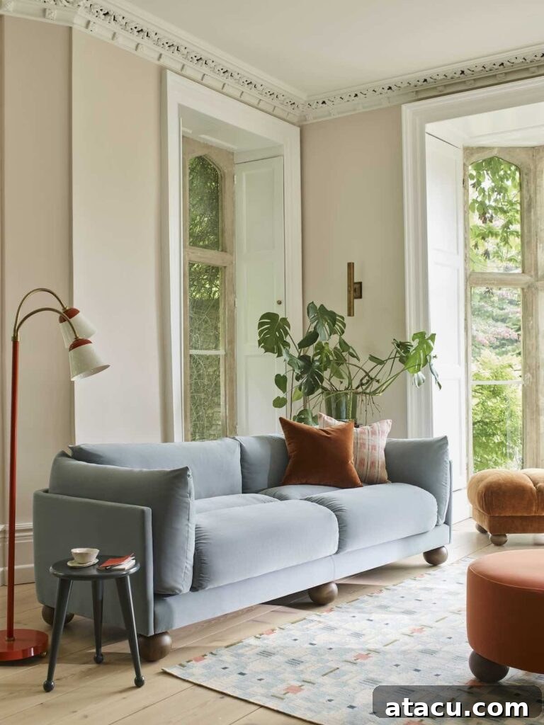 A cosy living room with magnolia walls, a soft blue sofa, and warm-toned pillows, featuring large windows with natural light and a mix of modern and vintage decor.