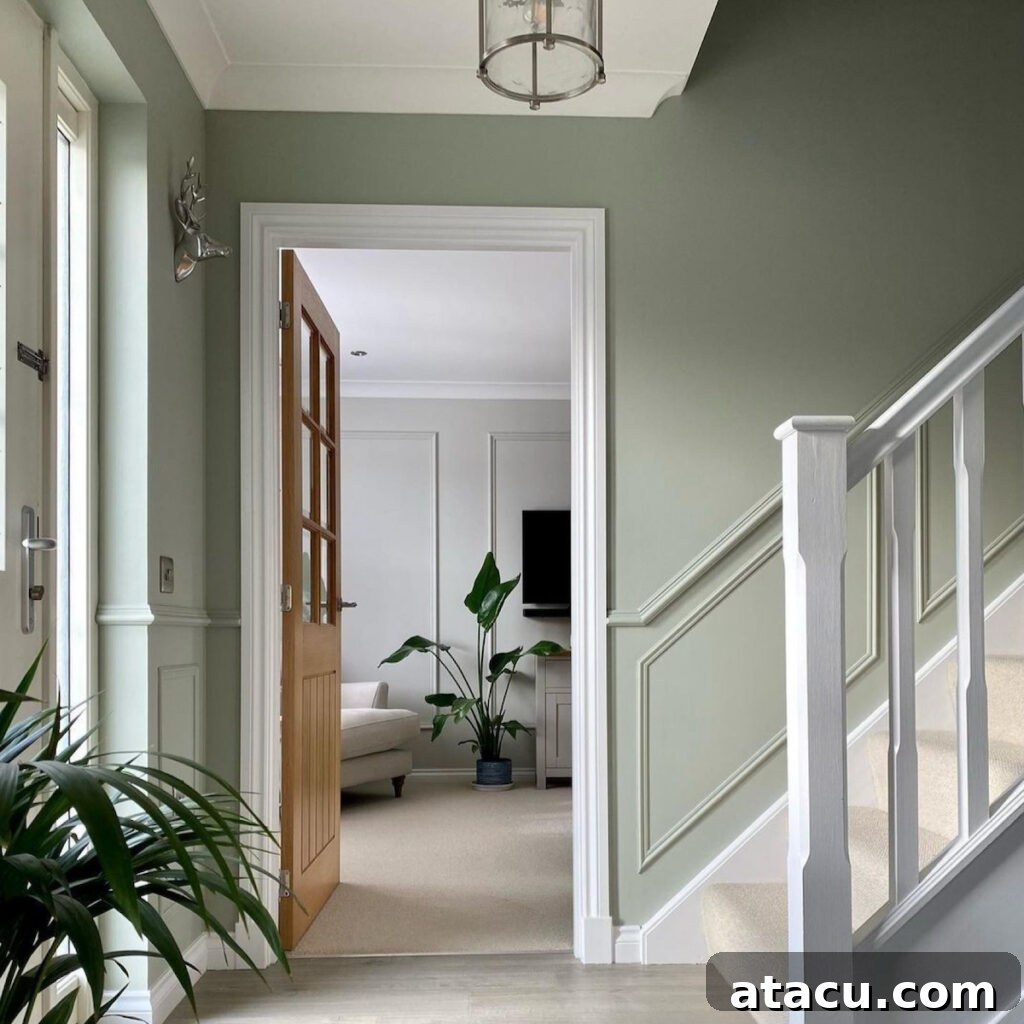 A stylish entryway with sage green walls, white trim, and a wooden door leading to a bright living space with neutral decor and a potted plant. A staircase with white railings adds depth to the design.