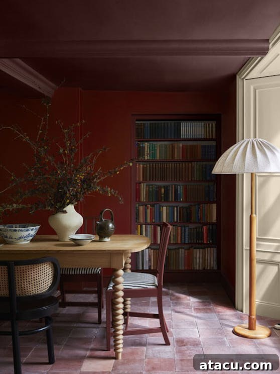 Ignite Your Interior: 8 Cherry Red Design Concepts 7 A cozy dining room with cherry red walls features a built-in bookshelf filled with colorful books. The space is styled with a wooden dining table, mismatched chairs, and a statement floor lamp with a fabric shade. A large vase with branches adds a natural touch, complementing the earthy tones of the terracotta floor tiles.