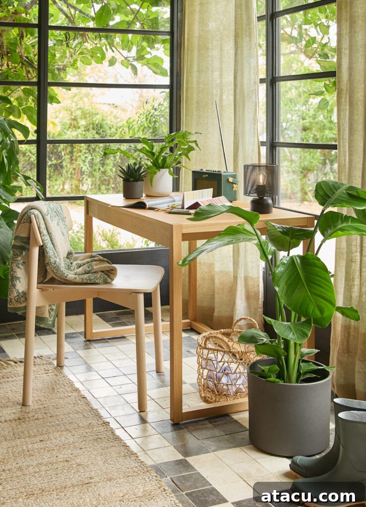 Cosy home office with a wooden desk, potted plants, and natural light streaming through large windows with green curtains. A beige chair with a patterned throw blanket sits next to the desk, which holds an open book, a lamp, and a vintage radio. A woven basket and green rubber boots rest on the tiled floor.