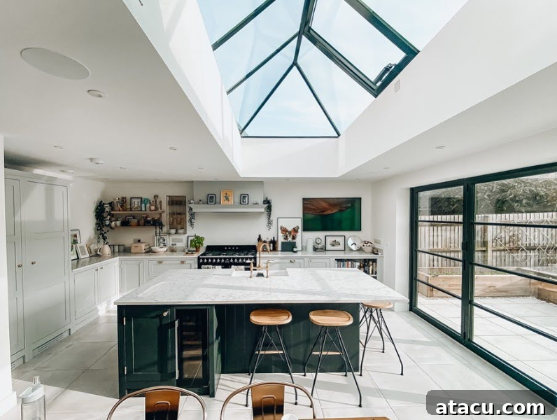 Modern kitchen with a glass roof lantern, marble island, and dark green cabinetry.