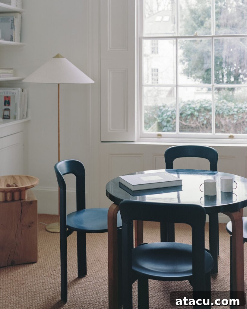 A dining space in a Georgian home renovation featuring a round black table, navy chairs, and a large window with garden views.