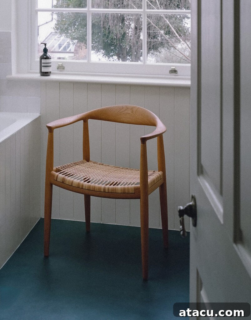A bright bathroom in a Georgian home renovation featuring a woven chair, deep green flooring, and a large sash window.