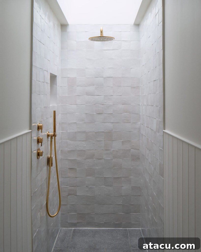 A minimalist shower in a Georgian home renovation with textured white zellige  tiles, brass fixtures, and a skylight.