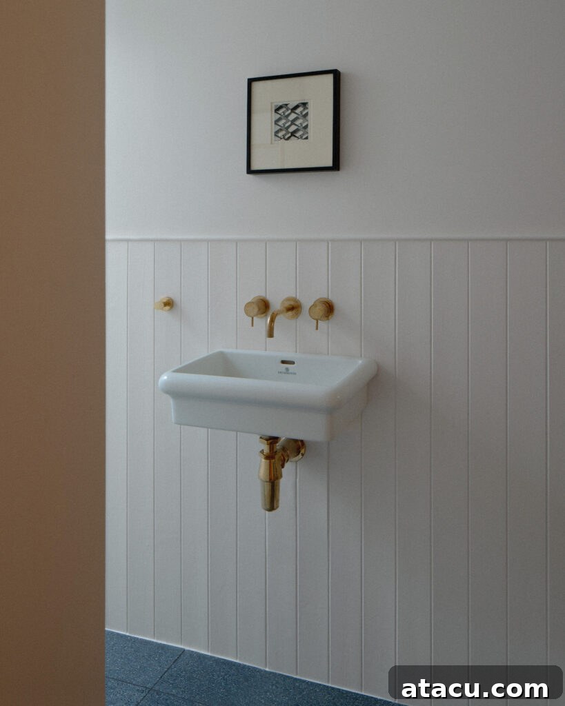 A minimalist bathroom sink in a Georgian home renovation with brass fixtures, white paneling, and a framed artwork.