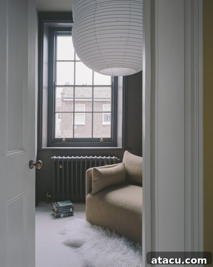 A cozy reading nook in a Georgian home renovation with dark walls, a plush armchair, and a large paper lantern.