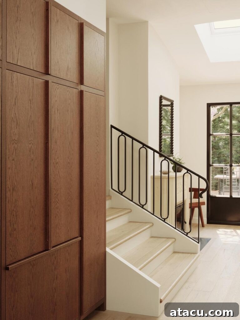 Modern staircase with an elegant iron railing, situated beside warm wood-paneled cabinetry and a sleek glass door, creating a sophisticated transition.