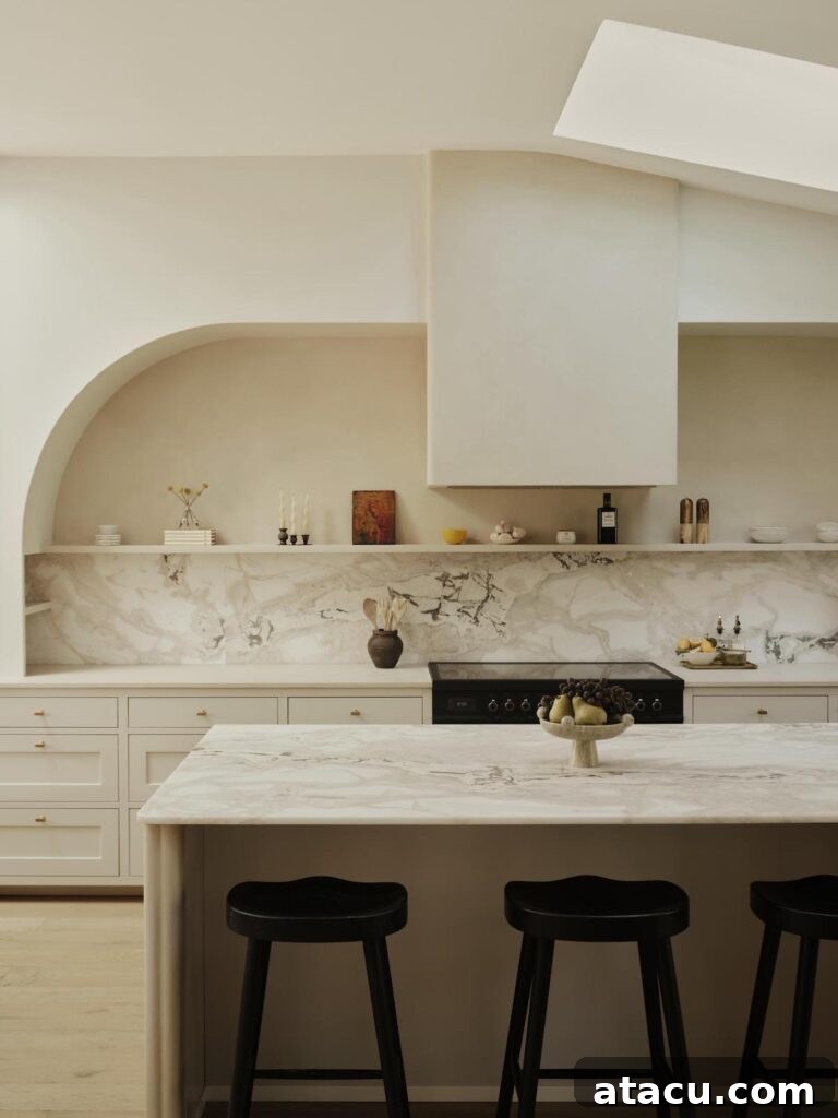 Spacious marble kitchen with an elegant arched shelf, a distinctive plaster hood, and a large central island accompanied by stylish black stools.