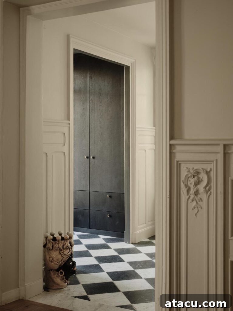 Elegant hallway in a renovated Parisian home featuring classic checkerboard marble flooring, modern dark built-in cabinetry, and original architectural details.
