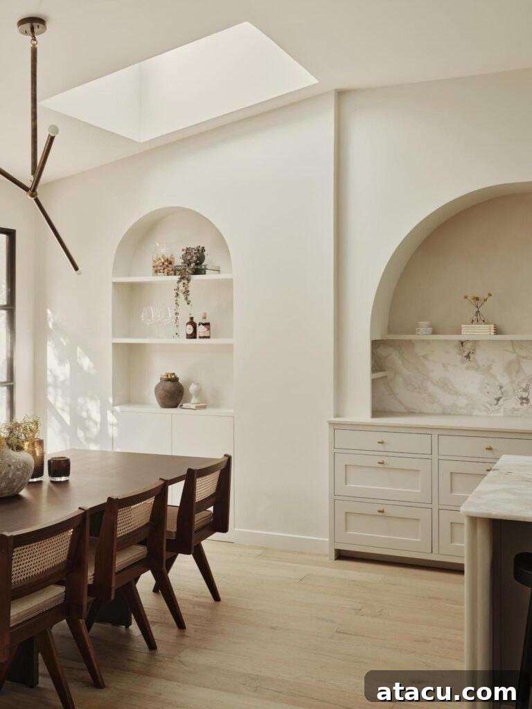 Minimalist dining room with a sleek wood table and elegant cane chairs, bathed in natural light from a large skylight.