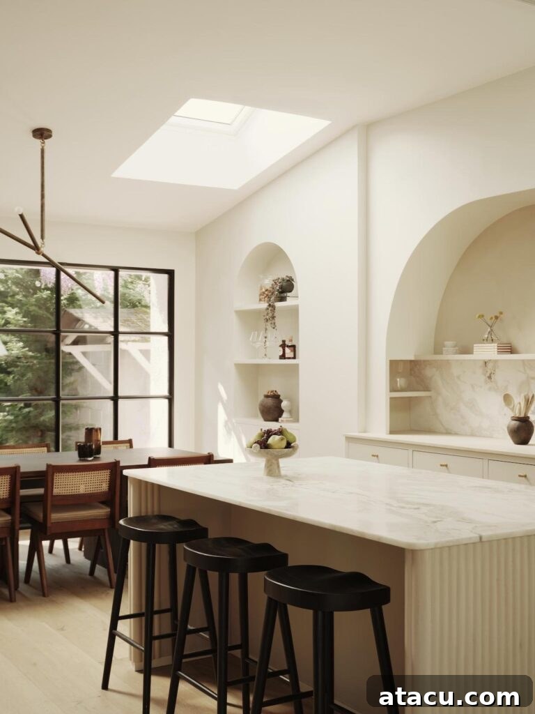 Bright and airy kitchen featuring a central marble island, elegant arched niches for storage and display, and chic black bar stools.