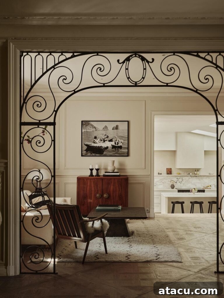 Eclectic sitting room featuring an ornate iron archway, a stylish mid-century chair, and a framed view of the adjacent marble kitchen.