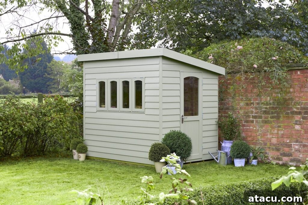 A pale green potting shed in the corner of a lawned garden.